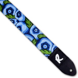 May include: A guitar strap with a repeating pattern of blue blueberries and green leaves on a light blue background. The strap has a black leather end piece with a white "R" logo.
