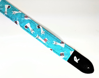 May include: A turquoise guitar strap with a white llama pattern and black leather ends. The strap has a white 'R' on the end.