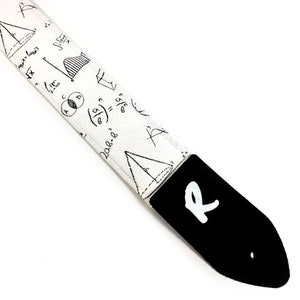 May include: White guitar strap with black mathematical equations and symbols printed on it. The strap has a black leather end with a white letter "R" printed on it.