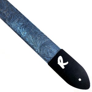 Peut inclure: Une sangle de guitare bleue avec un motif en relief floral et une extrémité en cuir noir avec un logo "R" blanc.