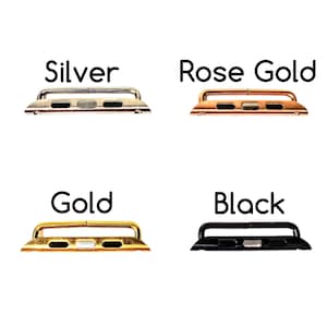 Puede incluir: Cuatro adaptadores de correa de reloj en plata, oro rosa, oro y negro. Cada adaptador tiene una base rectangular con una barra superior curva. Los colores est&aacute;n etiquetados con el texto "Silver", "Rose Gold", "Gold" y "Black".