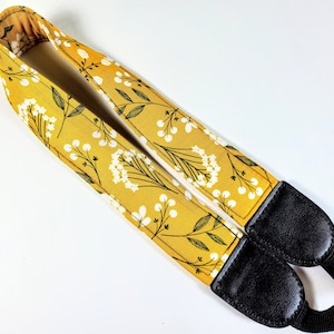 May include: A yellow camera strap with a white floral pattern and black adjustable straps.