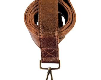 May include: A rolled-up, brown leather strap with a metallic bronze finish. The strap features a brass-colored clasp and buckle. The strap is designed for use with a bag or purse.
