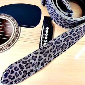 Könnte beinhalten: Ein braunes und schwarzes Gitarrengurt mit Leopardenmuster und einer Wildleder-ähnlichen Textur.