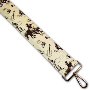 Könnte beinhalten: Cremefarbener Gurt mit einem sich wiederholenden Muster von Cowboy-Illustrationen in Braun. Das Design umfasst Cowboys, Gitarren, Stiefel und Pferde. Der Gurt hat Metallbeschläge.