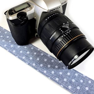 May include: A silver Pentax ZX-30 camera with a black lens. The camera is sitting on a blue and white polka dot fabric strap.