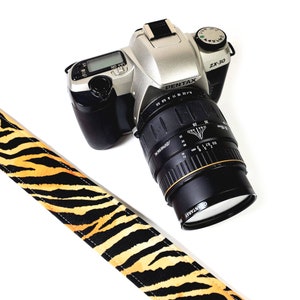 May include: A silver Pentax ZX-30 camera with a black lens and a tiger print camera strap.