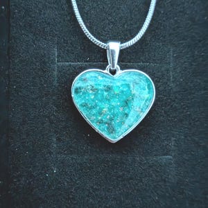 Peut inclure: Un collier pendentif en forme de cœur avec une incrustation en résine turquoise vif contenant des paillettes irisées. Le pendentif est entouré d'un cadre en métal argenté poli et est suspendu à une chaîne serpent assortie en métal argenté.