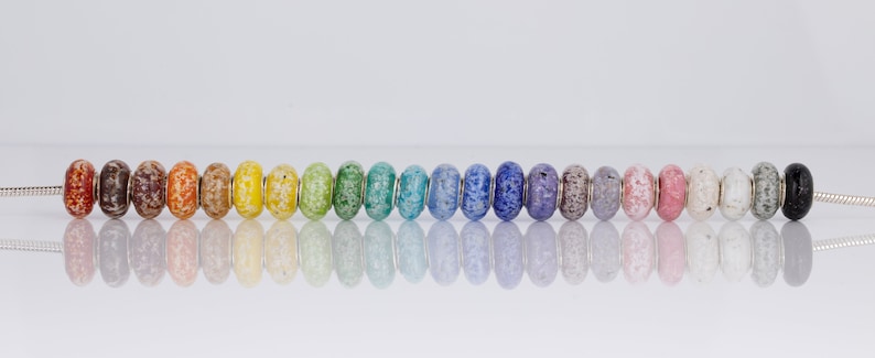 Op de afbeelding: Een regenboogassortiment van 20 kleine glazen kralen met een gespikkeld patroon. De kralen zijn geregen aan een zilveren ketting.