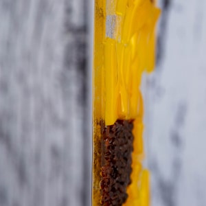 Puede incluir: Primer plano de una pieza de arte de resina amarilla y marr&oacute;n. La pieza est&aacute; hecha de m&uacute;ltiples capas de resina, con una superficie texturizada. La pieza tiene forma de flor, con un centro marr&oacute;n y p&eacute;talos amarillos.
