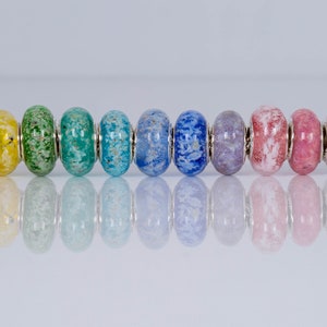 Op de afbeelding: Een regenboog van kleurrijke glazen kralen met zilveren accenten op een zilveren ketting. De kralen zijn bespikkeld met witte vlekken.