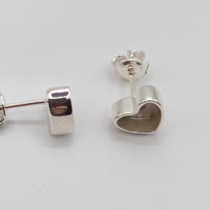 May include: Two silver heart-shaped stud earrings. The earrings are made of a shiny, reflective metal. The heart shape is simple and smooth, with a slightly rounded form. The posts and backs are also silver.