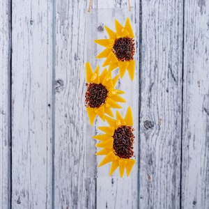 Puede incluir: Un panel de vidrio con tres girasoles amarillos de vidrio. Los girasoles est&aacute;n hechos de peque&ntilde;os trozos de vidrio y tienen centros marrones.
