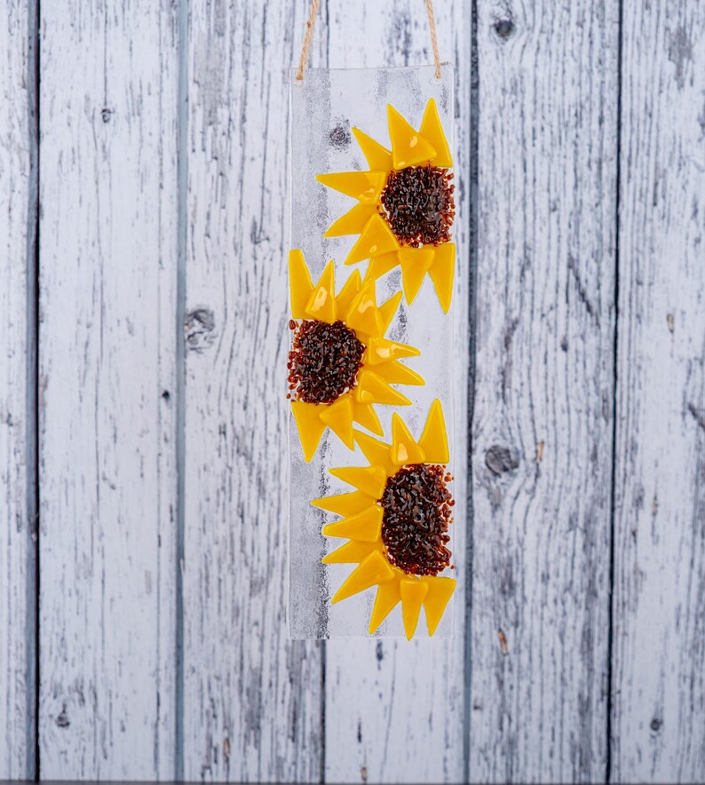 Puede incluir: Un panel de vidrio con tres girasoles amarillos de vidrio. Los girasoles est&aacute;n hechos de peque&ntilde;os trozos de vidrio y tienen centros marrones.
