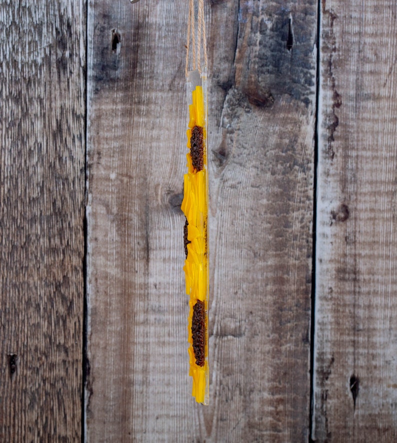 Puede incluir: Una suspensi&oacute;n de pared vertical de acr&iacute;lico con una cuerda para colgar. El acr&iacute;lico est&aacute; lleno de girasoles secos, con los p&eacute;talos amarillos hacia afuera y los centros marrones hacia adentro.