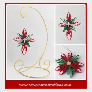 May include: Three red and green paper quilled Christmas ornaments in the shape of a star. The ornaments are hanging from a gold metal stand. The website www.Neverboredcreations.com is displayed at the bottom of the image.