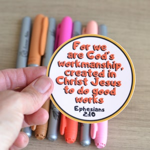 May include: A round sticker with a yellow border and orange text that reads "For we are God's workmanship, created in Christ Jesus to do good works Ephesians 2:10".