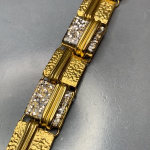 Puede incluir: Pulsera de tono dorado con eslabones rectangulares. Cada eslabón tiene una superficie dorada texturizada y una pieza central con un acabado plateado brillante.