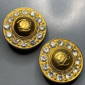 May include: A pair of gold-tone earrings with clear rhinestones surrounding a gold-tone disc with the initials "HL" engraved in the centre.