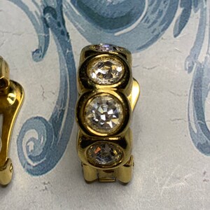 Op de afbeelding: Gouden clip-on oorbellen met drie heldere ronde strass steentjes.