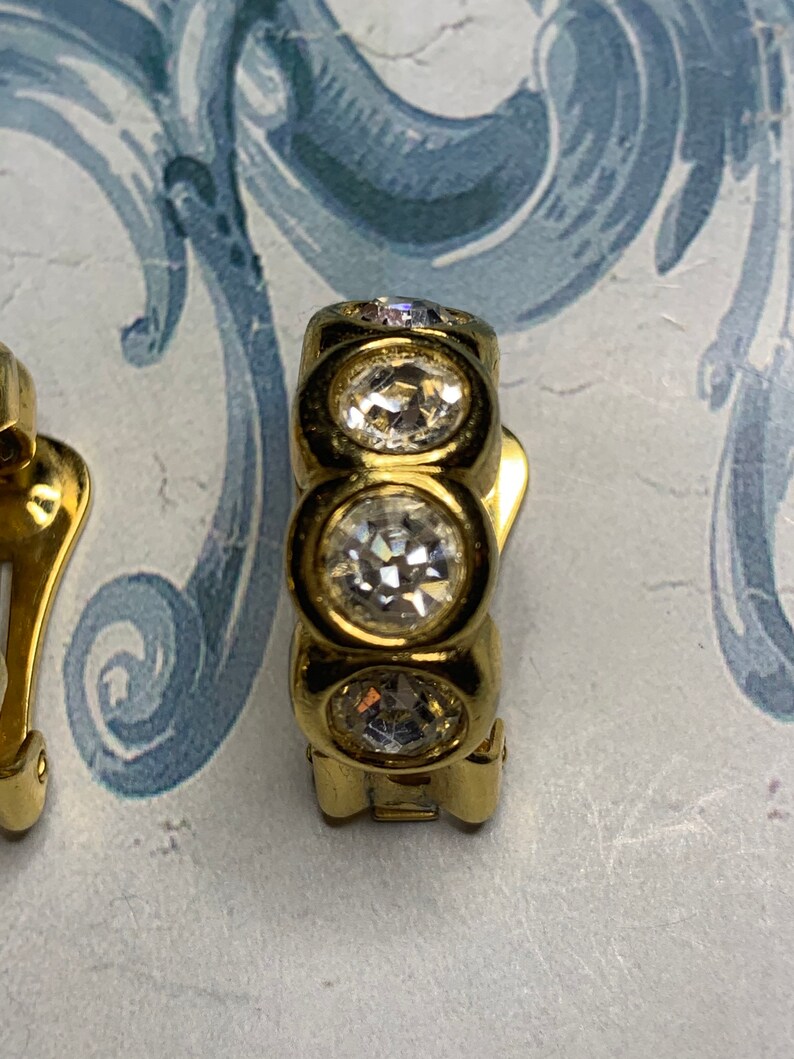 Op de afbeelding: Gouden clip-on oorbellen met drie heldere ronde strass steentjes.