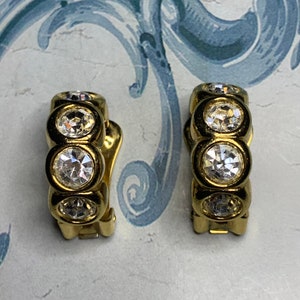 Op de afbeelding: Een paar gouden creolen met heldere strass-accenten. De oorbellen hebben een scharnier sluiting.