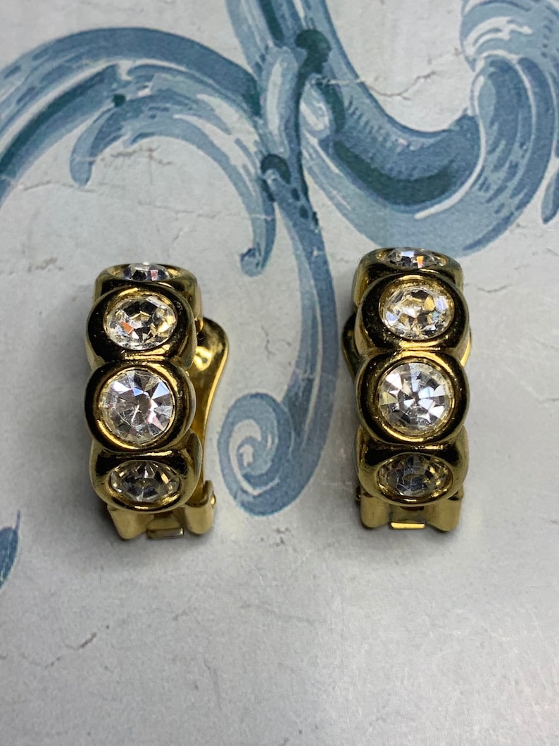 Op de afbeelding: Een paar gouden creolen met heldere strass-accenten. De oorbellen hebben een scharnier sluiting.