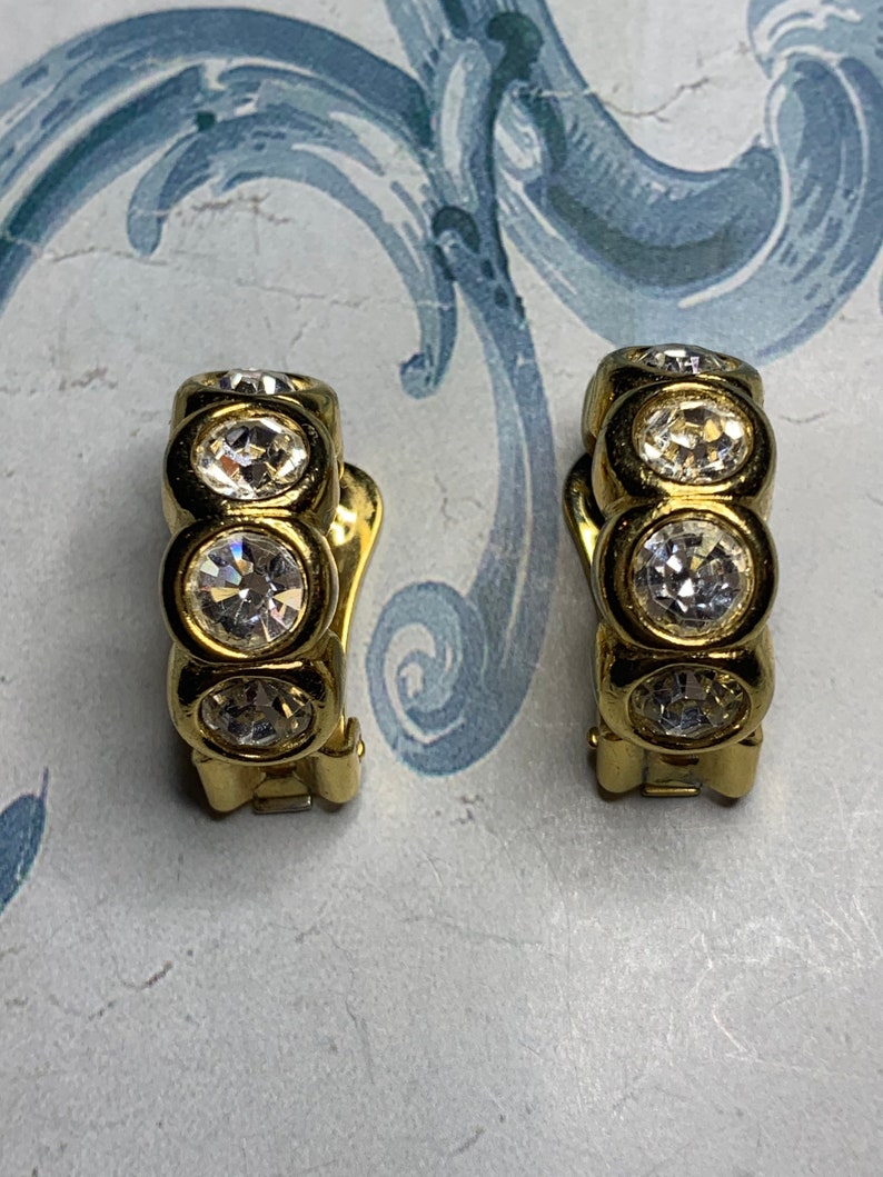 Op de afbeelding: Een paar gouden creolen met heldere strass-accenten.
