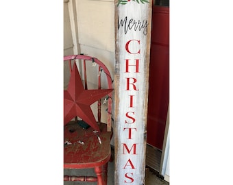 Puede incluir: Un letrero de madera rústico con las palabras "Merry Christmas" en letras negras y rojas. El letrero está pintado de blanco con un acabado envejecido y detalles de acebo verde. Una estrella y una silla rojas se ven en el fondo.