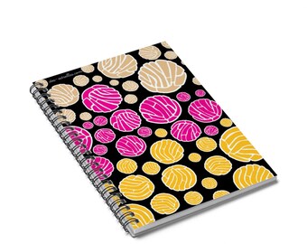 May include: A black spiral notebook with a colorful pattern of pink, yellow, and beige pastry-like shapes. The notebook has a white spiral binding and the text "dos-estrellas.com" is printed in white on the cover.