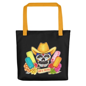 May include: A black tote bag with yellow straps features a colorful illustration of a sugar skull wearing a cowboy hat and surrounded by popsicles. The text "Viva el Paletero" is written on a banner below the skull.