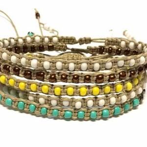 May include: Five layered bracelets with brown, white, yellow, and turquoise beads. The bracelets are made of hemp cord and are tied together with a knot.