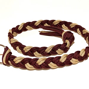 May include: Braided keychain wrist strap in burgundy and tan. The strap is made of tightly woven cord, with a tassel at one end and a silver-colored key ring at the other. The design features a repeating pattern of the two colors.