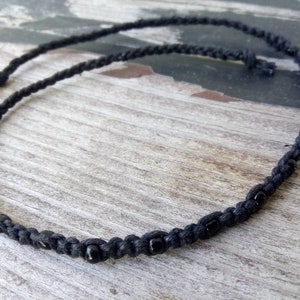 May include: A black braided cord necklace with small black beads.