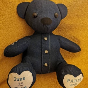 Pu&ograve; includere: Un orsacchiotto di jeans blu con occhi neri e naso nero. L'orso indossa una camicia di jeans con bottoni. I piedi dell'orso hanno cuori ricamati con il testo "June 25 Dave" e "Paris 2001".
