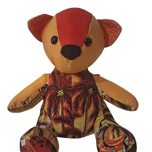 May include: A stuffed teddy bear constructed from patchwork fabric. The head features a red center panel with tan sides and dark ears. The body and limbs are made from a tropical-themed fabric displaying palm trees and sunset-colored patterns.