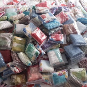 May include: A large pile of colourful crocheted squares, each individually packaged in clear plastic bags. The squares are made with different coloured yarns and patterns.