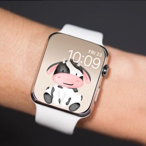以下が含まれることがあります： 画面に白黒の漫画の牛が描かれた白いApple Watch。時間は10:09で、日付は金曜日23日です。