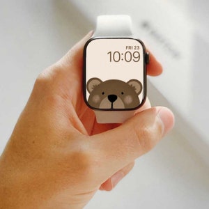 May include: A white Apple Watch with a brown bear face watch face. The time is 10:09 and the date is FRI 23.