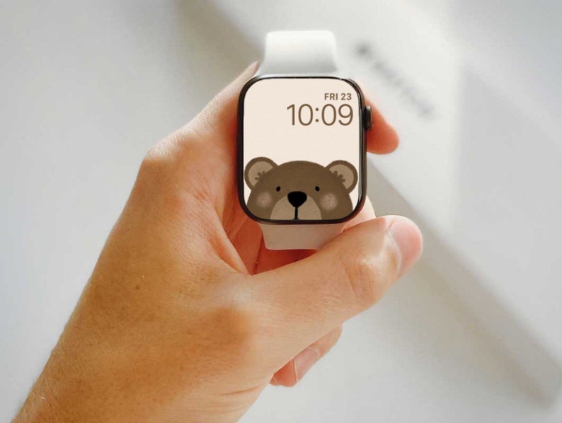 May include: A white Apple Watch with a brown bear face watch face. The time is 10:09 and the date is FRI 23.