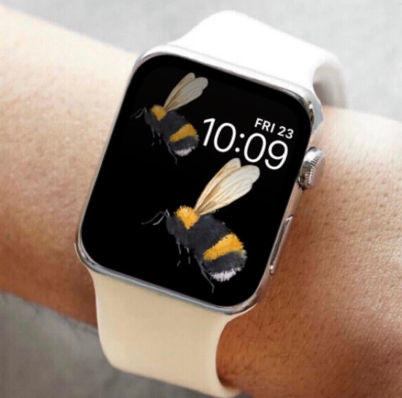 Peut inclure: Une Apple Watch blanche avec un cadran noir affichant l'heure 10:09 et la date VEN 23. Le cadran de la montre pr&eacute;sente une illustration d'abeille.