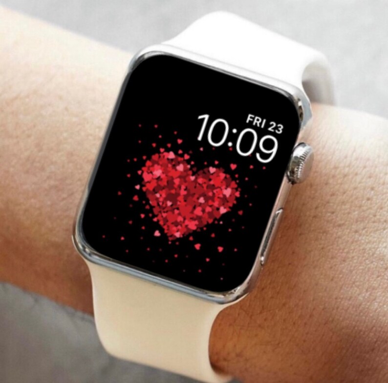 May include: White Apple Watch with a black face displaying the time 10:09 and the date FRI 23. The watch face has a red heart made of smaller red hearts.