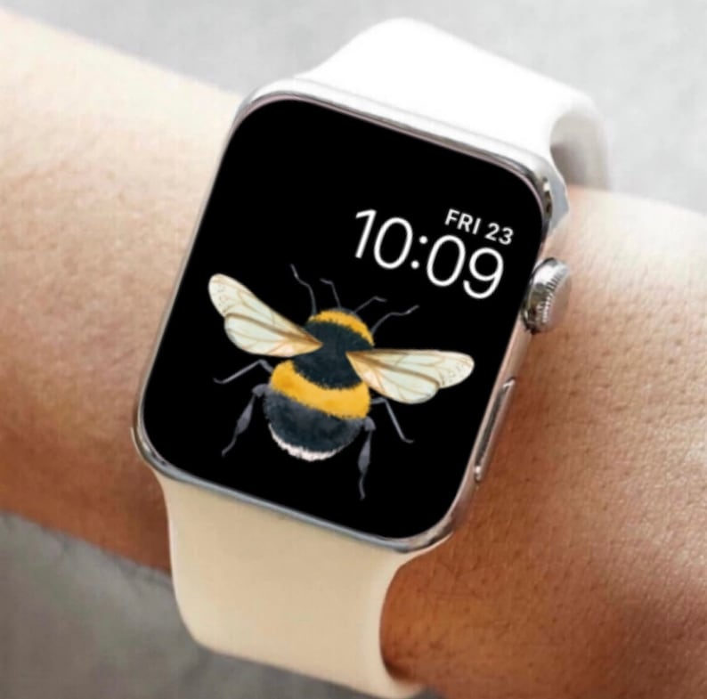 Peut inclure: Une Apple Watch blanche avec un cadran noir affichant l'heure 10:09 et la date VEN 23. Le cadran de la montre pr&eacute;sente un graphique d'un bourdon.