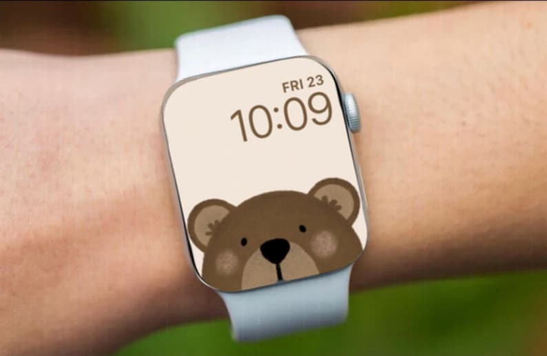 May include: A white Apple Watch with a brown bear face watch face. The time is 10:09 and the date is FRI 23.
