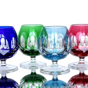 Puede incluir: Cuatro vasos de cristal con tallo y diseños tallados. Los vasos son en tonos de azul, verde y rojo.