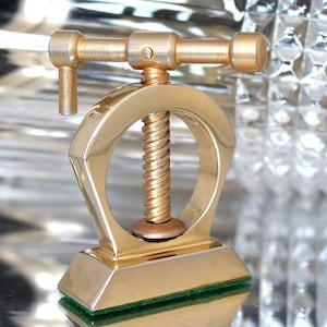 Peut inclure: Un casse-noisette doré avec un design décoratif. Le casse-noisette a un mécanisme à vis et une poignée.