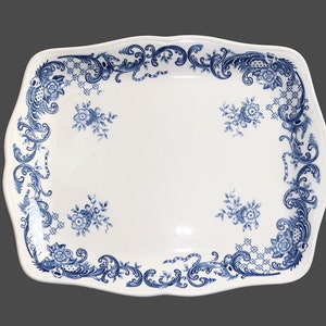 May include: A rectangular white ceramic serving platter with scalloped edges, featuring a blue floral pattern along the border and four small floral clusters scattered across the centre of the smooth, glossy surface.