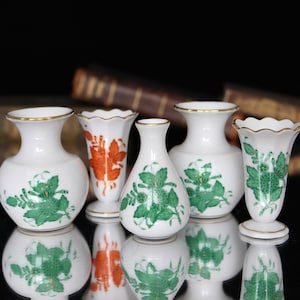 May include: Five small porcelain vases with floral designs. The vases are white with green and orange floral patterns. The vases are all different shapes and sizes.