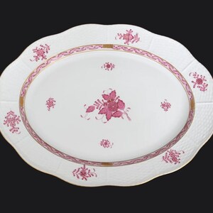 May include: A white oval serving platter with a pink floral design and a gold rim. The platter has a raised, textured edge.