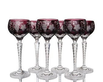 May include: A set of six wine glasses featuring deep purple bowls with etched grape and leaf patterns. Each glass has a clear, textured, faceted stem and a circular base with a radial pattern, standing against a plain white background.